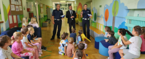 Policjanci wraz z Radnym rozmawiają z uczniami młodszych klas na szkolnym korytarzu