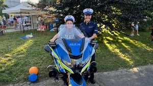 Chłopczyk na policyjnym motocyklu i stojąca obok funkcjonariuszka