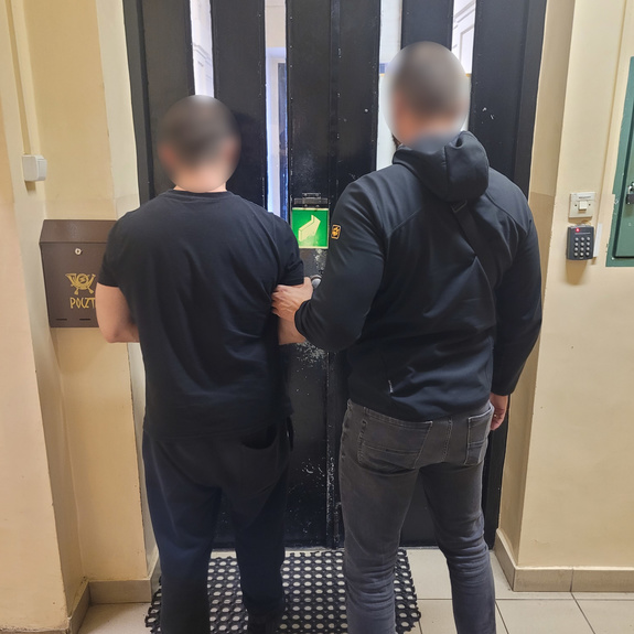 Policjant operacyjny prowadzi zatrzymanego mężczyznę