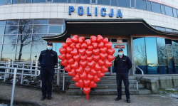 Dwaj policjanci stoją przed budynkiem Komisariatu Policji szóstego a pomiędzy nimi duże serce wykonane z czerwonych balonów