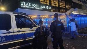 dwoje policjantów stojących przy oznakowanym radiowozie zaparkowanym przy stadionie