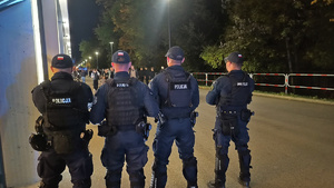 czterech umundurowanych policjantów stojących tyłem do zdjęcia przed stadionem