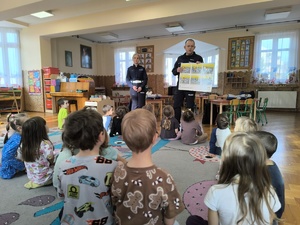 dzieci siedzące na dywanie, policjantka w tle