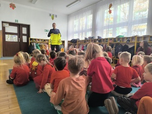 dzieci siedzą na dywanie, w tle policjant