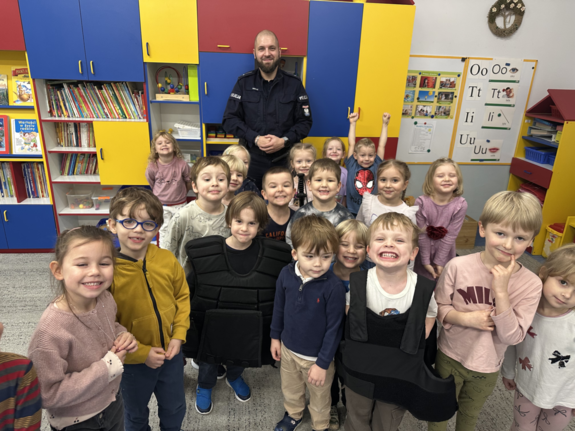 dzieci pozujące do zdjęcia, w tle policjant