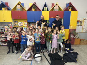 dzieci machają , w tle funkcjonariusze