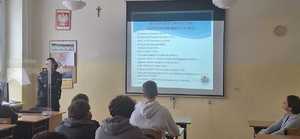 uczniowie w ławkach, policjantka w tle