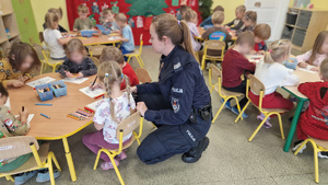 dzieci siedzące w ławkach i policjantka