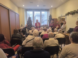 4 Seniorzy siedzą na sali, w tle mikołaj