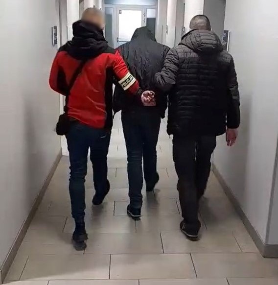 dwóch nieumundurowanych policjantów prowadzi zatrzymanego przez korytarz komisariatu