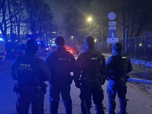 czterech umundurowanych policjantów biorących udział w zabezpieczeniu meczu stojących tyłem do zdjęcia