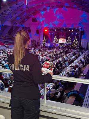 umundurowana policjantka trzymająca w ręce ulotkę obserwująca osoby siedzące przy stołach