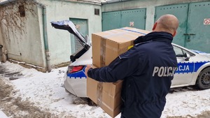 policjant przenosi do radiowozu paczki przeznaczone dla osób bezdomnych