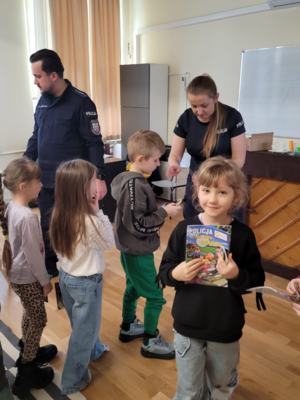 policjanci wręczają dzieciom ulotki informacyjne na temat bezpieczeństwa