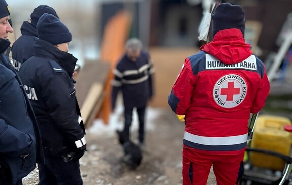 Umundurowani policjanci oraz przedstawiciel Polskiego Czerwonego Krzyża rozmawiają z mężczyzną