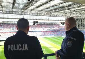 Dwóch umundurowanych policjantów obserwuje kibiców znajdujących się na stadionie