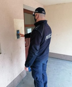 Policjant dzwoniący domofonem podczas kontroli osób przebywających na kwarantannie.