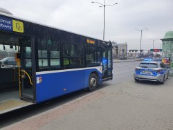 Policyjny radiowóz z włączonymi światłami uprzywilejowanymi oraz autobus.