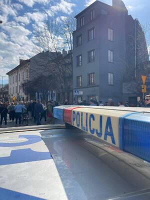 policyjne sygnały świetlne na dachu radiowozu, nad którymi widać osoby biorące udział w marszu