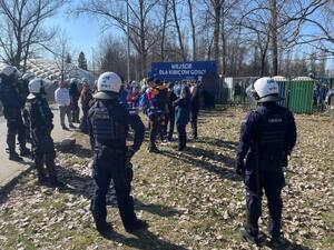 umundurowani policjanci obserwują kibiców zgromadzonych przy sektorze gości w rejonie stadionu