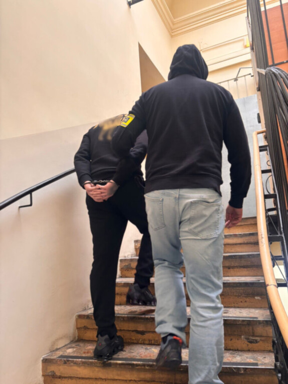 nieumundurowany policjant prowadzi osobę zatrzymaną z kajdankami założonymi na ręce trzymane z tyłu