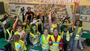 policjantka na wspólnym zdjęciu z dziećmi ubranymi w kamizelki odblaskowe i trzymającymi w dłoniach opaski odblaskowe