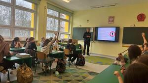 policjantka prowadząca prelekcję dla uczniów siedzących w ławkach