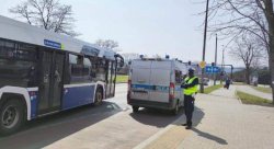 policjant stojący obok radiowozu i autobusu miejskiego