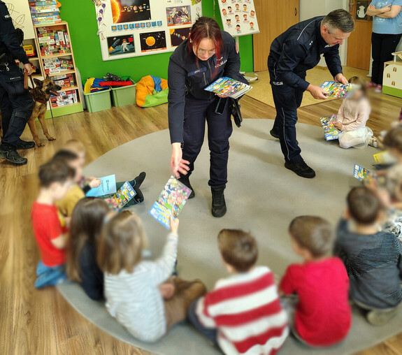 policjanci rozdają dzieciom książeczki edukacyjne o bezpieczeństwie