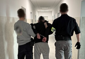 dwóch nieumundurowanych policjantów prowadzi zatrzymanego z kajdankami założonymi na ręce trzymane z tyłu