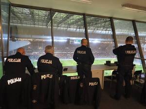 czterech umundurowanych policjantów obserwujących kibiców zgromadzonych na stadionie