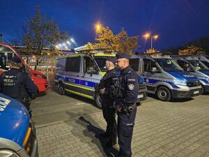 umundurowani policjanci stojący przed radiowozami zaparkowanymi przed stadionem