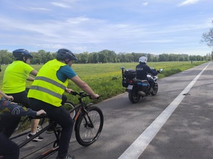 policjant na motocyklu eskortuje jadących na tandemie uczestników