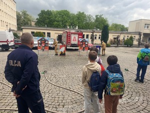 policjant i uczniowie przyglądają się pokazowi zorganizowanemu przez strażaków
