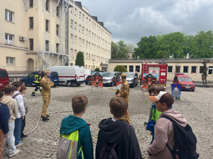 uczniowie przed budynkiem straży pożarnej słuchają strażaka opowiadającego o swojej pracy