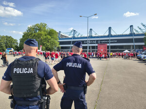 dwóch umundurowanych policjantów stojących tyłem do zdjęcia obserwują grupy przemieszczających się kibiców