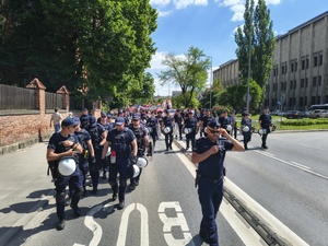 umundurowani policjanci idący jedną z głównych ulic miasta przed grupą osób biorących udział w marszu