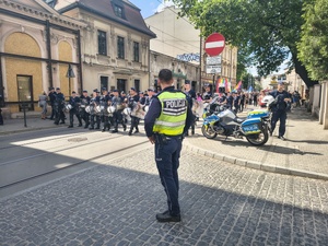 umundurowany policjant stojący przed policyjnym motocyklem oraz grupa policjantów idąca ulicą przed osobami biorącymi udział w marszu