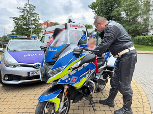 policjant stoi obok dziecka siedzącego na policyjnym motocyklu w tle radiowóz