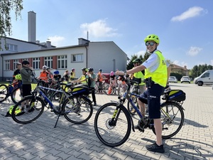 policjantka i uczestnicy przygotowujący się do przejazdu rowerowego przed budynkiem szkoły