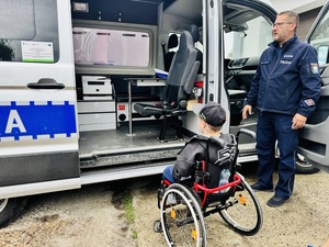 chłopiec siedzący na wózku inwalidzkim ogląda radiowóz w towarzystwie policjanta
