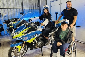 chłopiec z niepełnosprawnością i osoby mu towarzyszące, przy policyjnym motocyklu