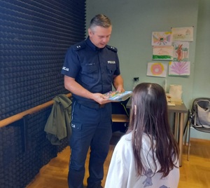 policjant wręcza dziecku ulotkę informacyjną o bezpieczeństwie