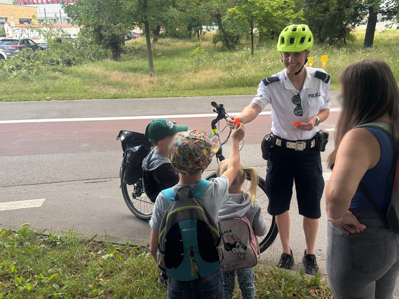 policjantka z patrolu rowerowego rozdaje dzieciom elementy odblaskowe