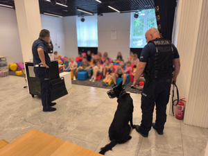policjant i policyjny przewodnik psa opowiadają o swojej pracy dzieciom spędzającym wakacje w ramach półkolonii