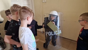 dziecko mające na sobie elementy policyjnego wyposażenia oraz inne dzieci stojące obok