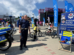 policjant ruchu drogowe w tle dzieci jadące na owerach po przygotowanym miasteczku rowerowym