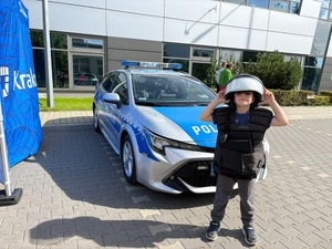 dziecko ubrane w elementy wyposażenia policyjnego, za nim radiowóz