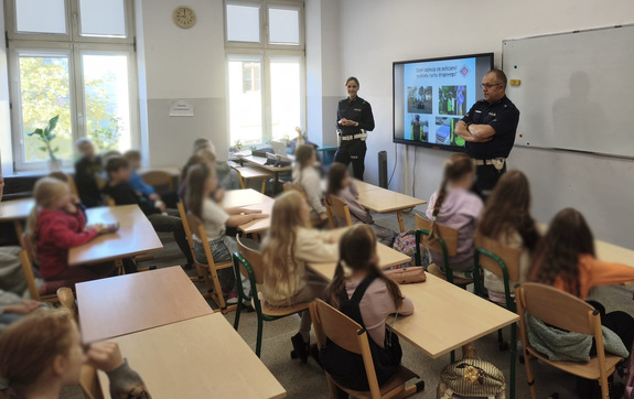 policjant z policjantką w sali lekcyjnej prowadzą prelekcję dla uczniów szkoły podstawowej