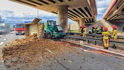 czynności ratownicze na miejscu wypadku drogowego na autostradzie A4. Uszkodzony samochód ciężarowy, który uderzył w filar estakady, na jezdni rozsypana ziemia z przewróconej wywrotki.